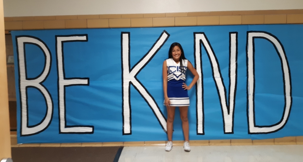 CIS student standing in front of be kind sign